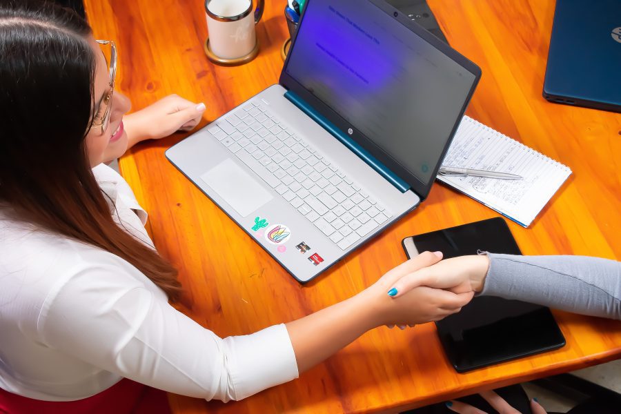 Two people doing a handshake, with a desk, laptop and mug on the background