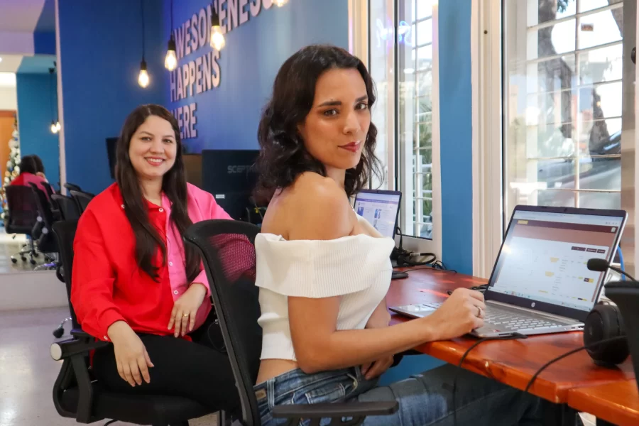 Two women sitting on a desk and working with laptops