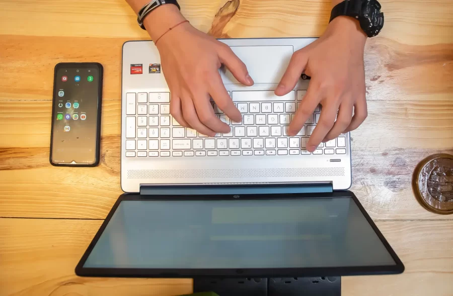 Hands writing on a computer with a phone next to it