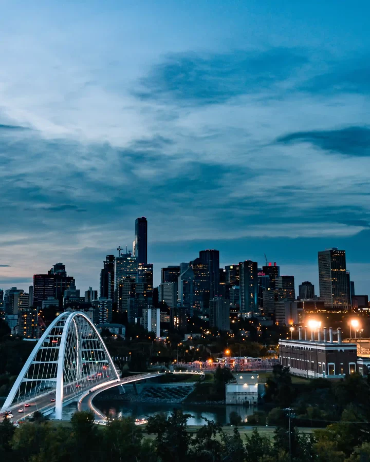 Evening view of downtown Edmonton, Alberta, Canada, featuring the Walterdale Bridge illuminated with city lights and a modern skyline in the background.