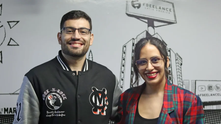 Two smiling bilingual Freelance Latin America remote professionals standing in front of the company's branded wall.